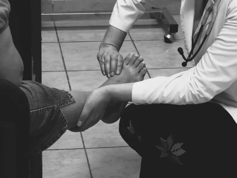 A clinician in a white coat holding a patient’s foot to examine it, in black and white