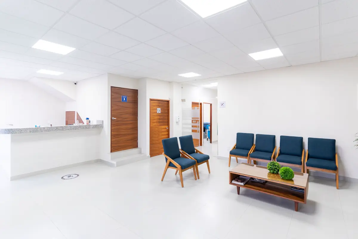 A bright, step-free clinic waiting area with blue armchairs, a low table and a reception counter